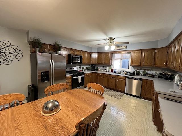 kitchen with a ceiling fan, appliances with stainless steel finishes, a sink, light countertops, and light floors