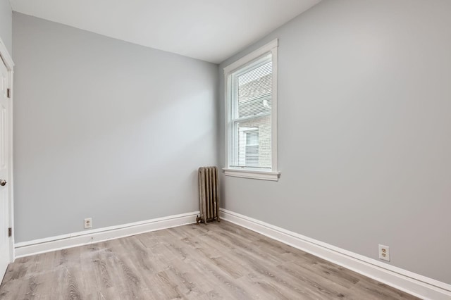 empty room featuring wood finished floors, baseboards, and radiator