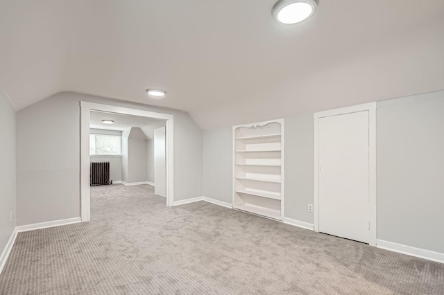 additional living space with carpet, baseboards, vaulted ceiling, radiator heating unit, and built in shelves