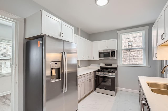 kitchen featuring a sink, appliances with stainless steel finishes, light countertops, baseboards, and marble finish floor