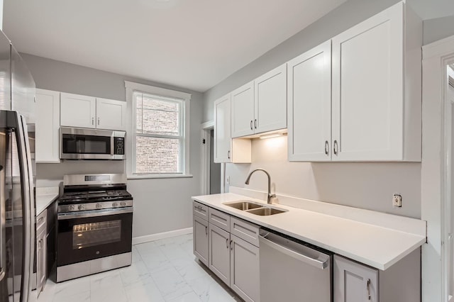 kitchen featuring stainless steel appliances, light countertops, marble finish floor, a sink, and baseboards