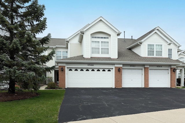 view of front facade featuring a garage, driveway, roof with shingles, and brick siding