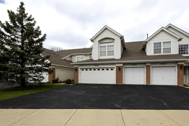 view of front of home with brick siding, an attached garage, roof with shingles, and aphalt driveway