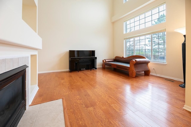 sitting room featuring light wood-style floors, baseboards, a fireplace, and a towering ceiling