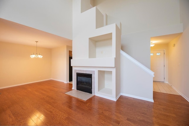 unfurnished living room featuring a towering ceiling, a chandelier, wood finished floors, and a tile fireplace
