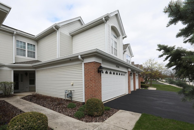 view of home's exterior featuring an attached garage, driveway, and brick siding