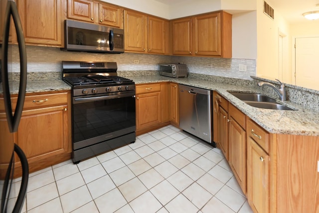 kitchen with tasteful backsplash, a sink, light stone counters, a toaster, and stainless steel appliances