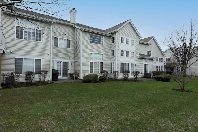 rear view of property featuring a lawn, central AC, and a chimney