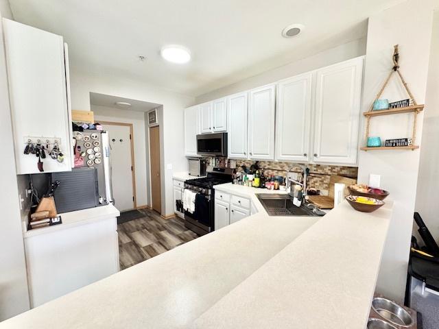 kitchen with decorative backsplash, white cabinets, stainless steel appliances, light countertops, and light wood finished floors