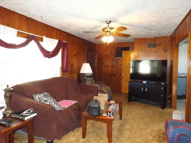 carpeted living room featuring visible vents, wood walls, and ceiling fan