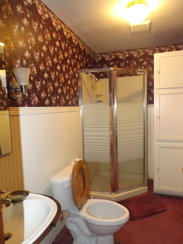 bathroom with wallpapered walls, wainscoting, toilet, and a shower stall