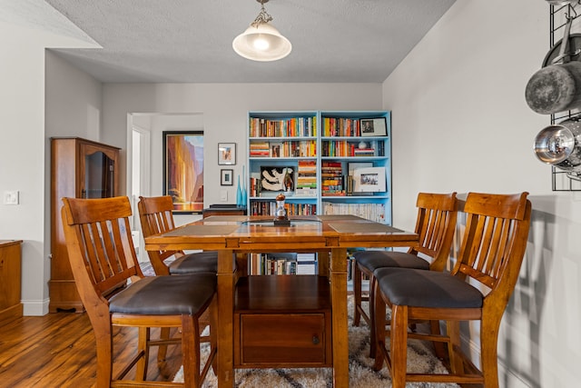 dining area with baseboards, a textured ceiling, and wood finished floors