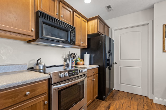 kitchen with brown cabinetry, visible vents, dark wood-style floors, light countertops, and black appliances
