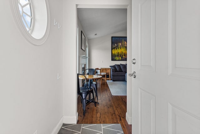 hallway with baseboards, vaulted ceiling, and wood finished floors