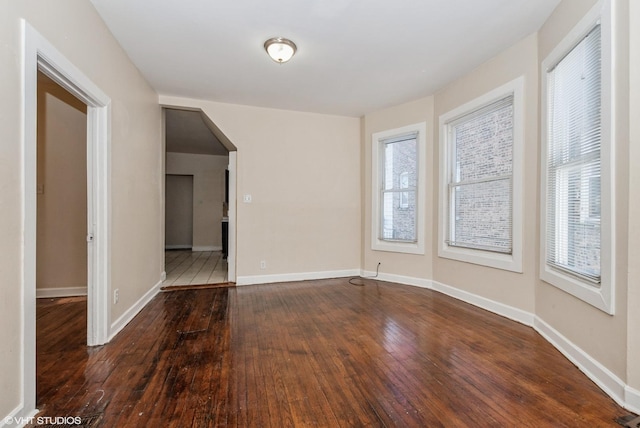 empty room with arched walkways, hardwood / wood-style floors, and baseboards