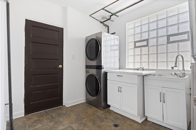 laundry room featuring stacked washer and clothes dryer, cabinet space, baseboards, and stone finish flooring