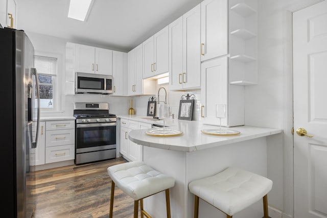 kitchen featuring appliances with stainless steel finishes, a peninsula, open shelves, and white cabinetry