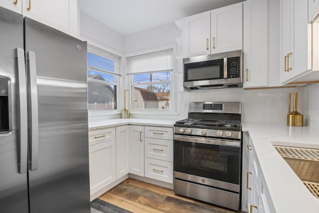 kitchen with appliances with stainless steel finishes, white cabinets, wood finished floors, and tasteful backsplash