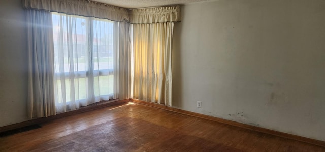 spare room with visible vents, baseboards, wood finished floors, and a wealth of natural light