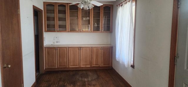 interior space featuring glass insert cabinets, ceiling fan, brown cabinetry, and dark wood finished floors