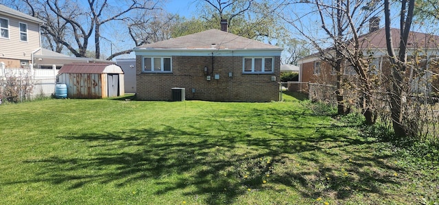 back of property with a storage shed, a lawn, central AC unit, brick siding, and fence