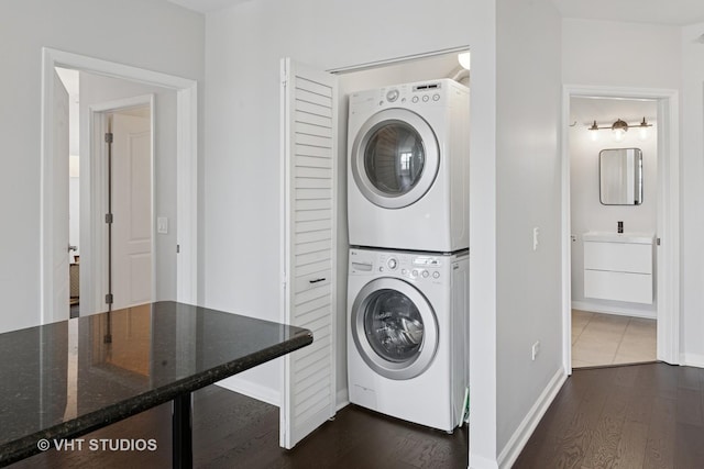 washroom featuring stacked washing machine and dryer, dark wood-type flooring, and baseboards