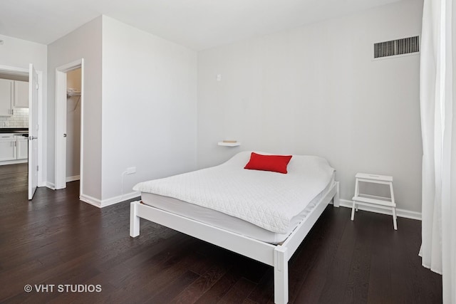 bedroom with dark wood-type flooring, baseboards, and a walk in closet