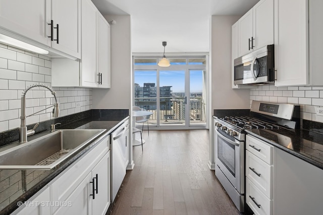 kitchen featuring stainless steel appliances, a sink, white cabinetry, dark wood-style floors, and backsplash