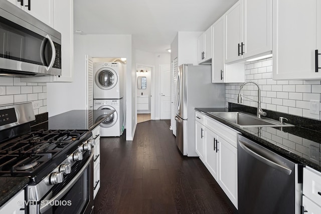 kitchen with stainless steel appliances, stacked washer and clothes dryer, a sink, white cabinets, and dark wood-type flooring