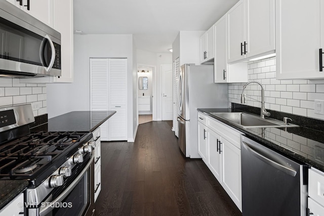 kitchen featuring appliances with stainless steel finishes, a sink, white cabinets, dark wood-style floors, and decorative backsplash