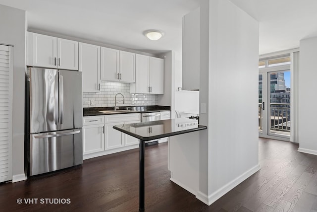 kitchen featuring appliances with stainless steel finishes, a sink, dark countertops, decorative backsplash, and dark wood-type flooring