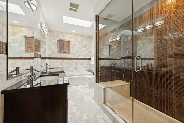 full bath featuring marble finish floor, tile walls, a shower stall, a sink, and a skylight