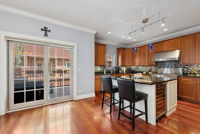 kitchen featuring brown cabinetry, ornamental molding, dark countertops, a breakfast bar area, and extractor fan