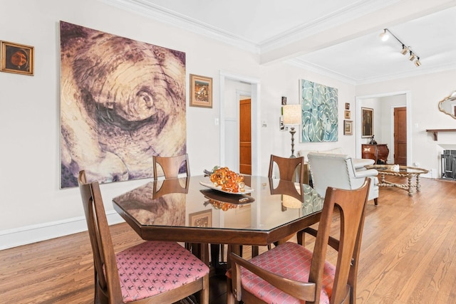 dining space with crown molding, light wood finished floors, and track lighting