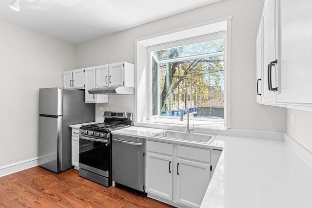 kitchen featuring appliances with stainless steel finishes, a sink, dark wood-style floors, under cabinet range hood, and white cabinetry