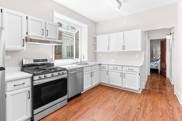 kitchen with light countertops, under cabinet range hood, white cabinets, a sink, and appliances with stainless steel finishes