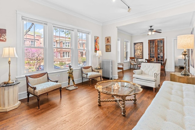 living area with crown molding, wood finished floors, baseboards, radiator heating unit, and rail lighting