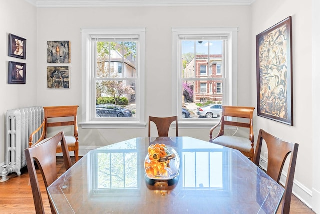 dining area featuring baseboards, ornamental molding, radiator, and wood finished floors