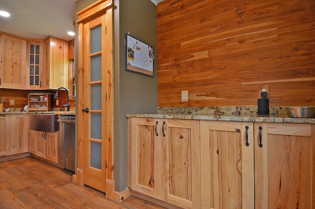 kitchen featuring light brown cabinetry, wood finished floors, light stone countertops, and glass insert cabinets