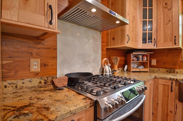 kitchen featuring tasteful backsplash, glass insert cabinets, stainless steel gas range oven, light stone countertops, and exhaust hood