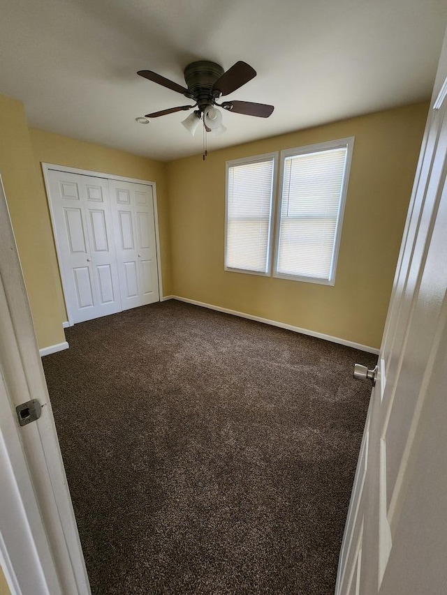 unfurnished bedroom with a closet, ceiling fan, dark colored carpet, and baseboards