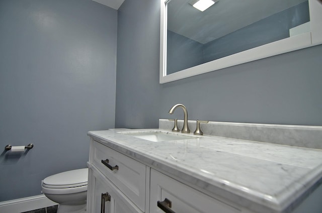 half bathroom featuring vanity, toilet, and baseboards
