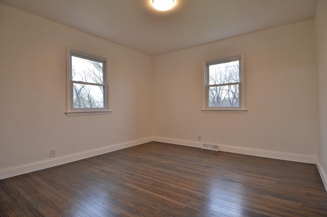 empty room with dark wood-type flooring, visible vents, baseboards, and plenty of natural light