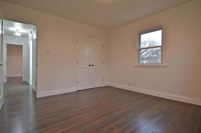unfurnished bedroom featuring dark wood-style floors, a closet, and baseboards