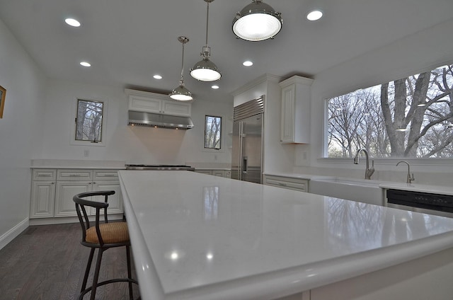 kitchen with built in refrigerator, white cabinets, under cabinet range hood, and light countertops