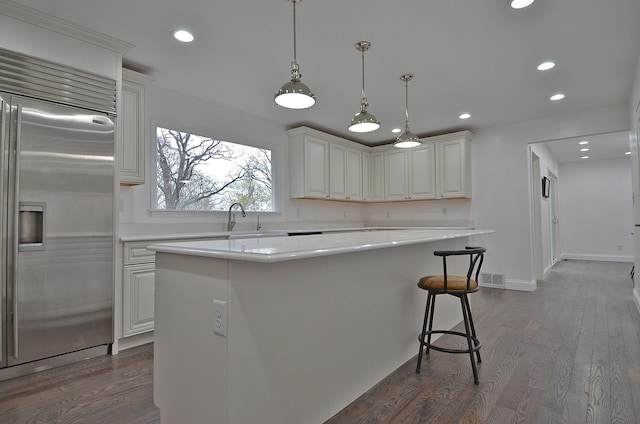 kitchen with dark wood finished floors, stainless steel built in fridge, a kitchen island, light countertops, and a sink