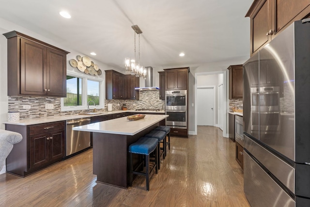 kitchen with wall chimney range hood, appliances with stainless steel finishes, a sink, decorative backsplash, and a kitchen bar