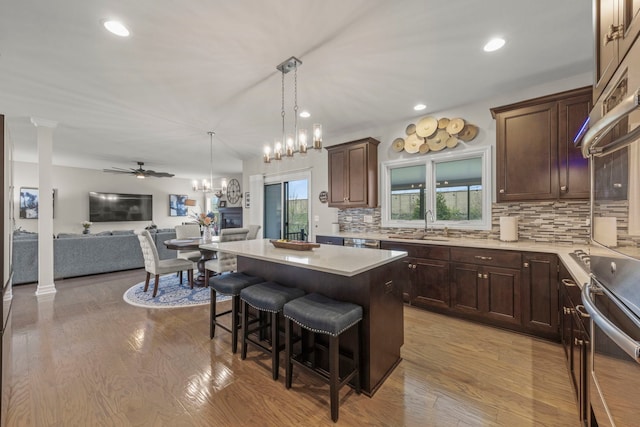 kitchen featuring dark brown cabinetry, backsplash, a kitchen island, light wood finished floors, and a breakfast bar