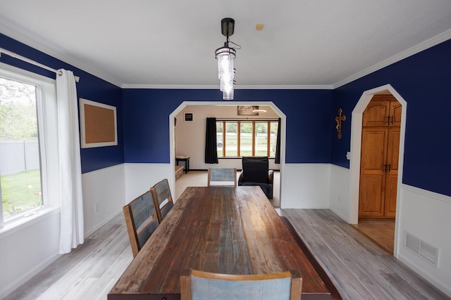 unfurnished dining area featuring ornamental molding, light wood-type flooring, visible vents, and arched walkways