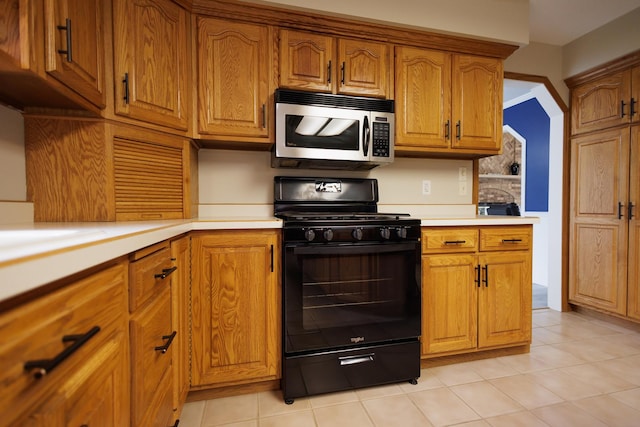 kitchen featuring light countertops, black gas range, stainless steel microwave, and brown cabinetry